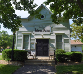 The Wheeling Historical Museum building's white siding and dark front doors in the daylight.